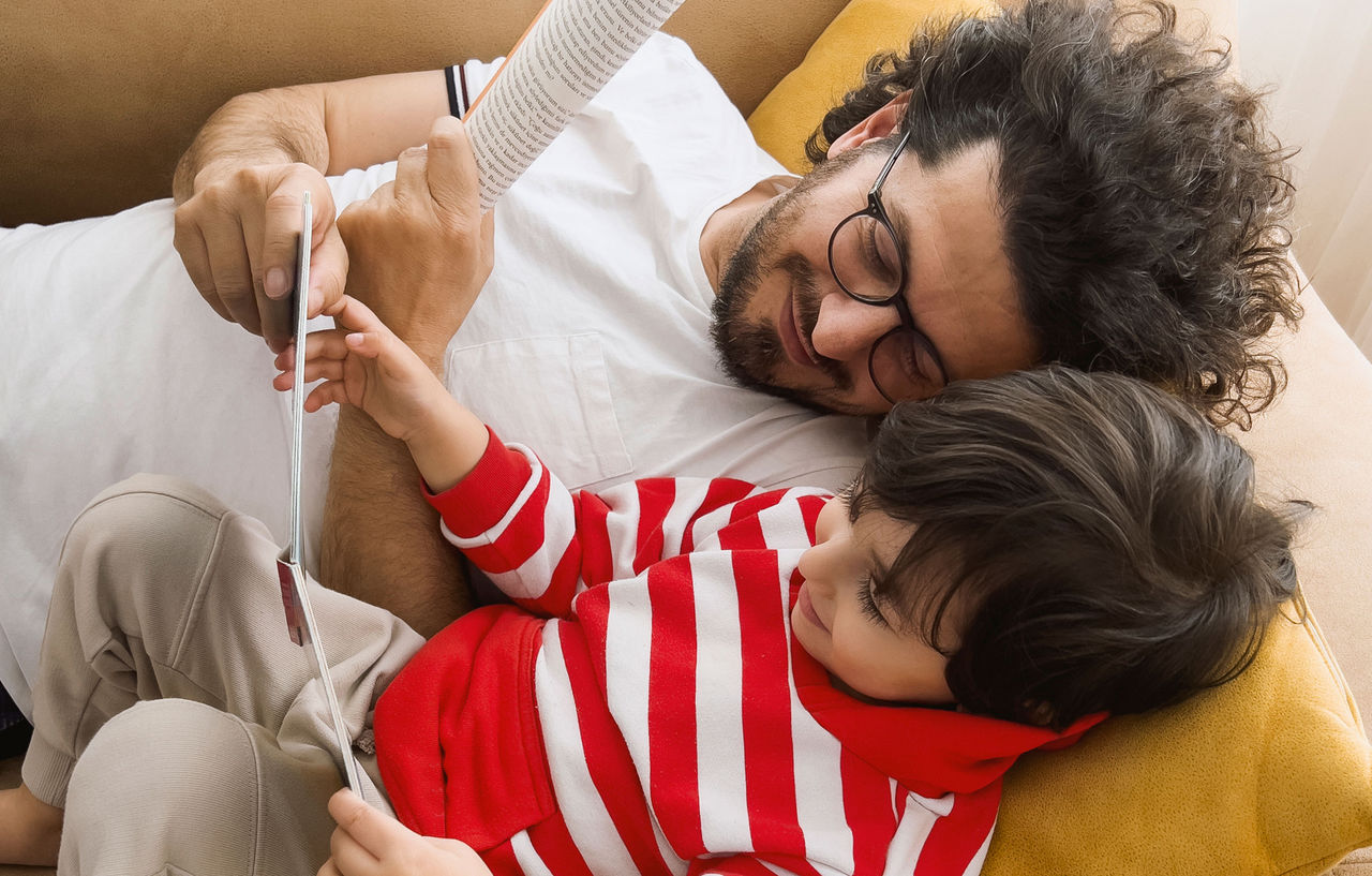 A father and son lying on the couch looking at a book