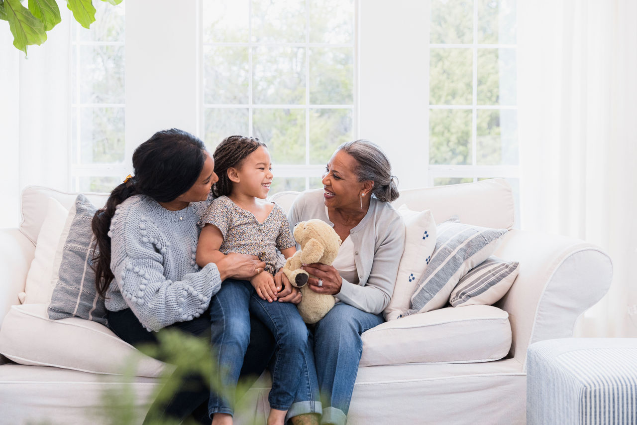 A mother, daughter and grandmother sitting on a couch together smiling