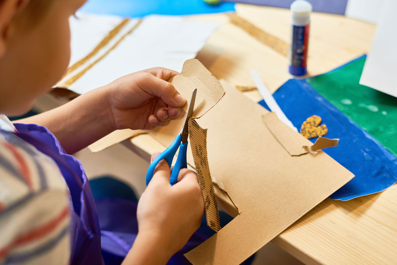 A child cutting a piece of cardboard with child-safe scissors