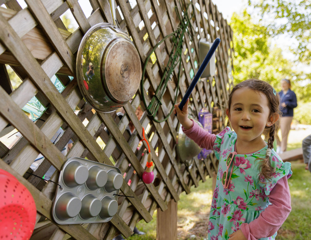 A child playing outdoors on a music wall created out of found objects like a muffin tin, colander and metal pot