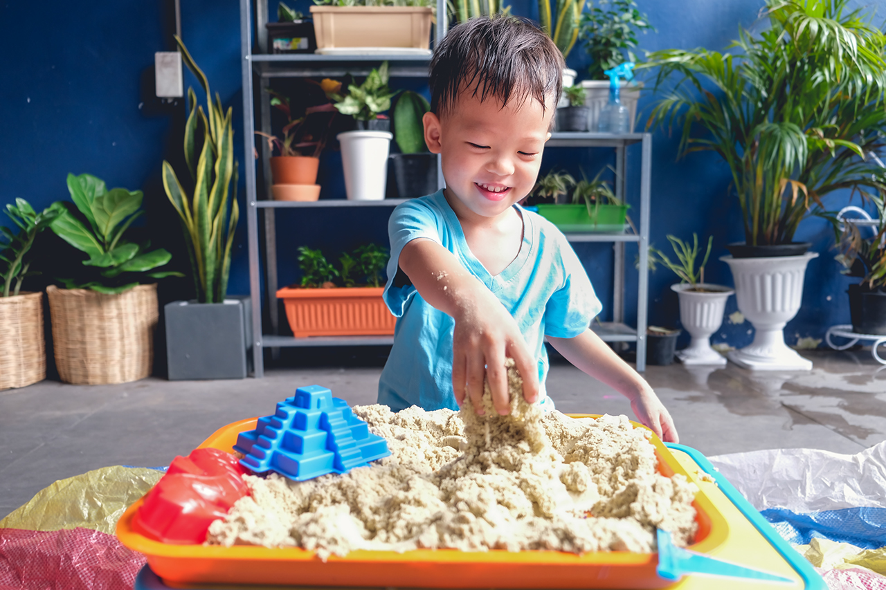 Cute smiling Asian toddler boy playing with kinetic sand in sandbox