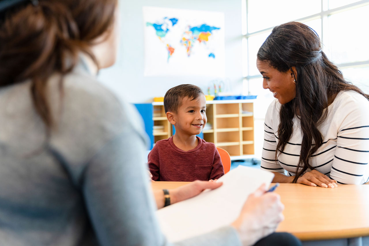 teachers sitting with a young boy at a table in a preschool classroom