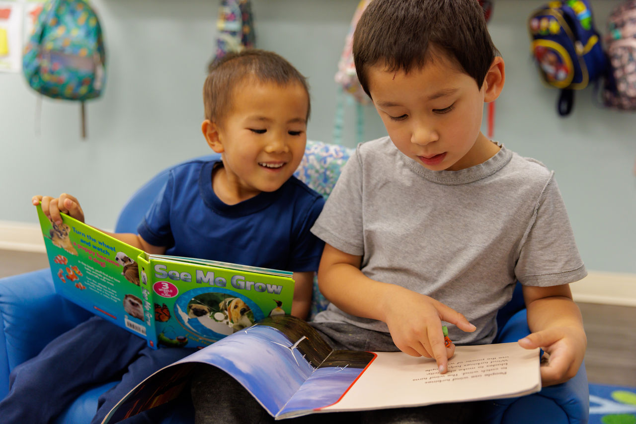 Two children sitting next to each other reading books together