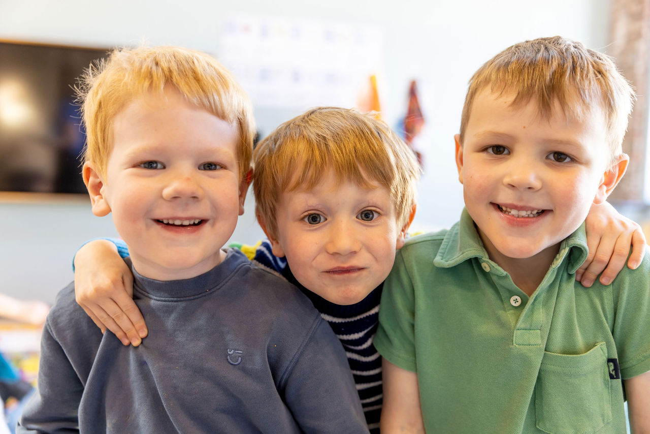 Three boys standing together two smiling and one making a funny face