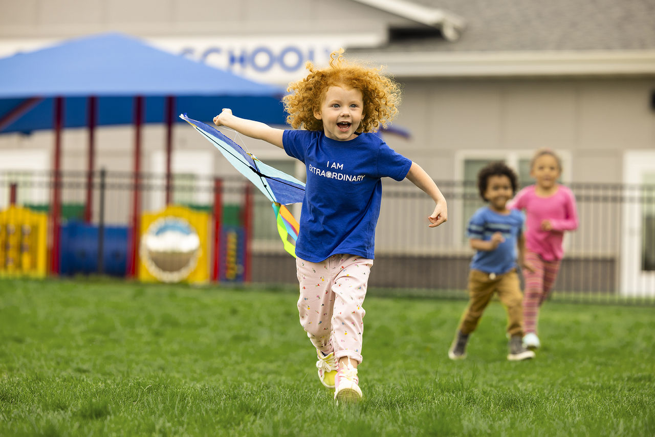 Child running with a kite on a preschool playground