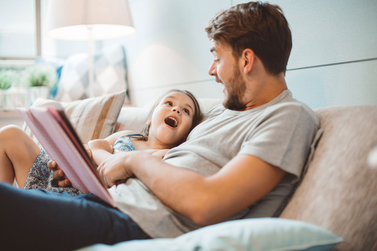 Dad and preschool age child read together on a couch