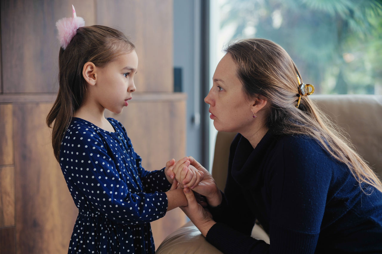 A woman holding hands and speaking with a young girl