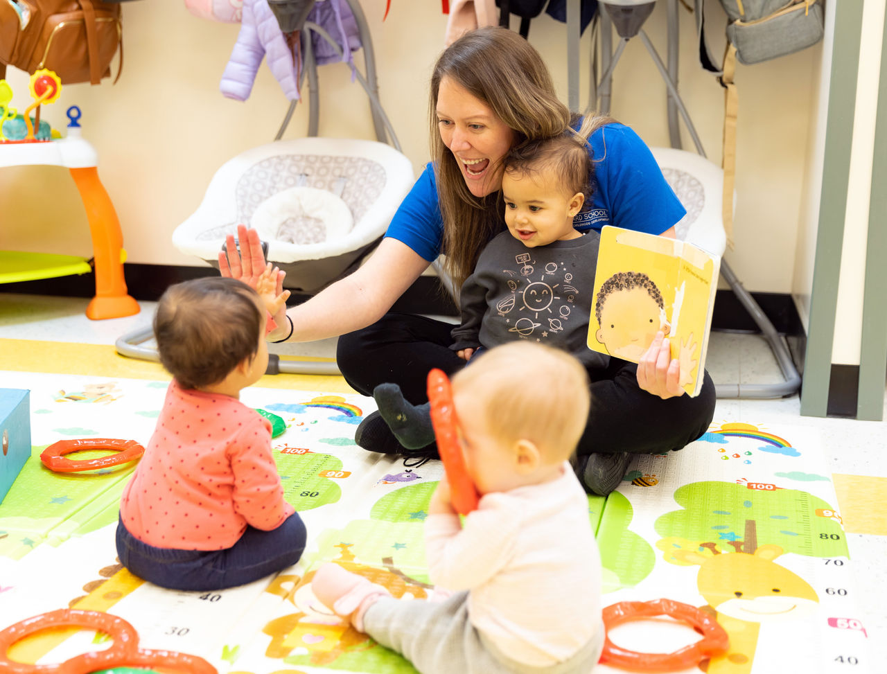 A teacher sitting and reading a book to a group of infants in a preschool classroom