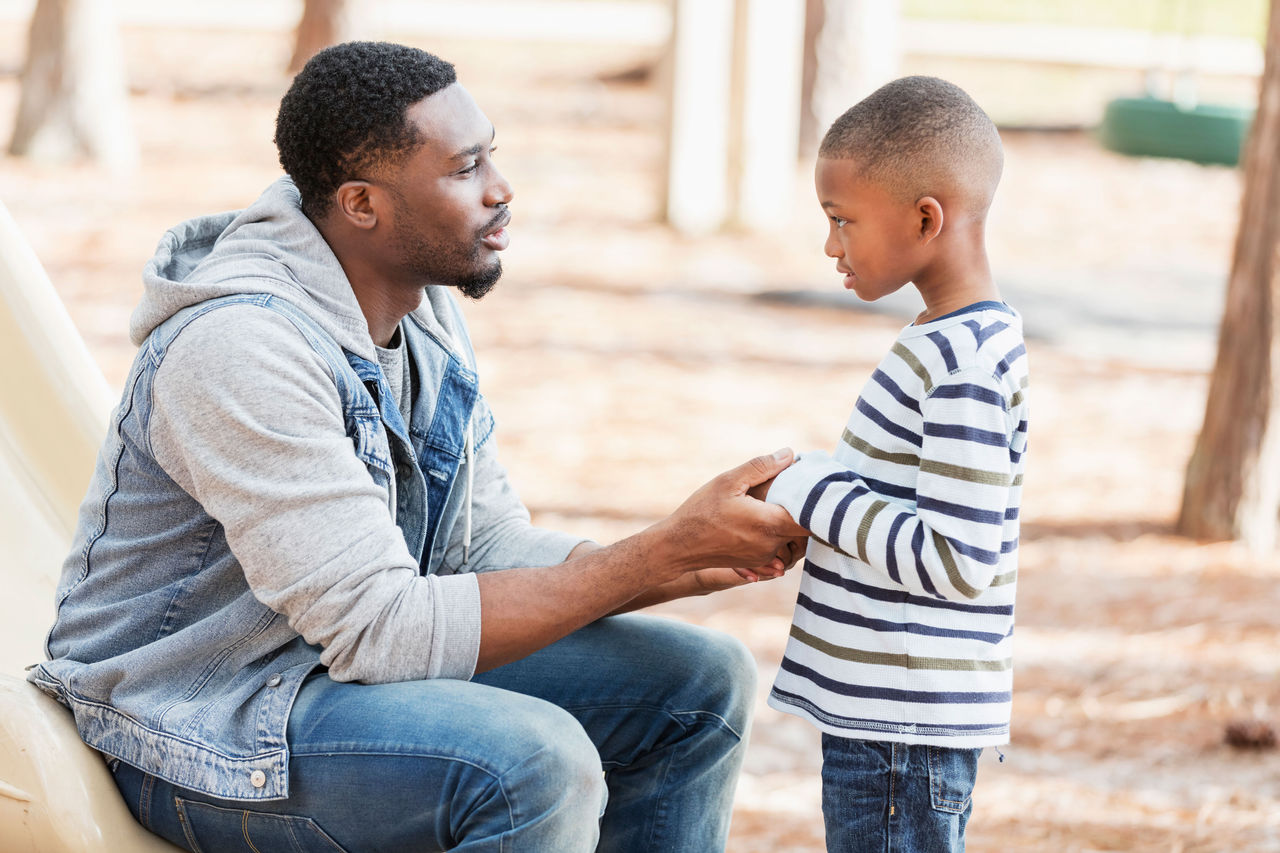 A father speaking to his son while holding his hands