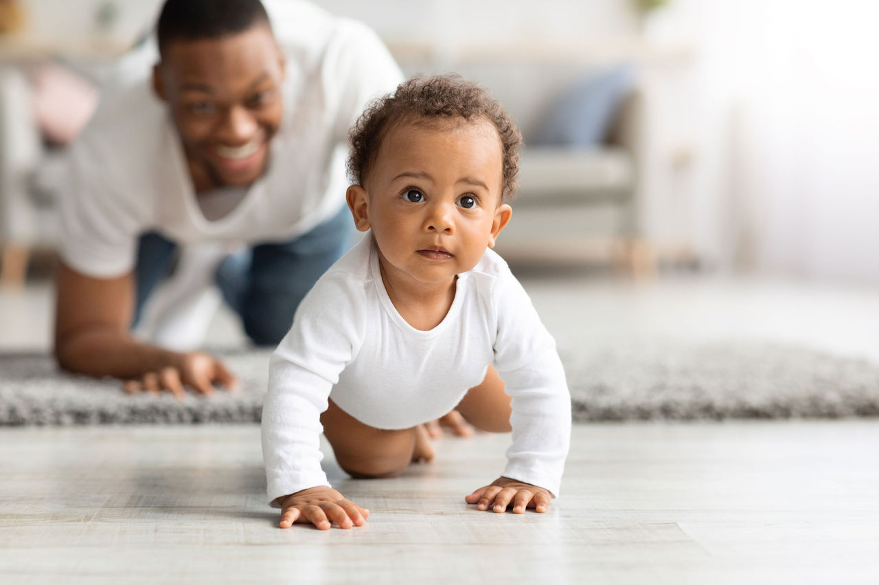 A baby crawling while the father watches from behind