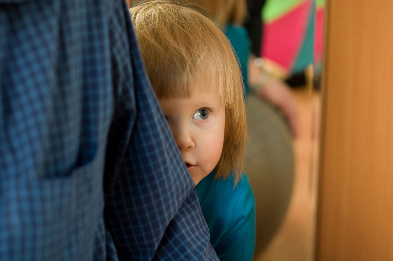 A small child peeking out from behind an adult