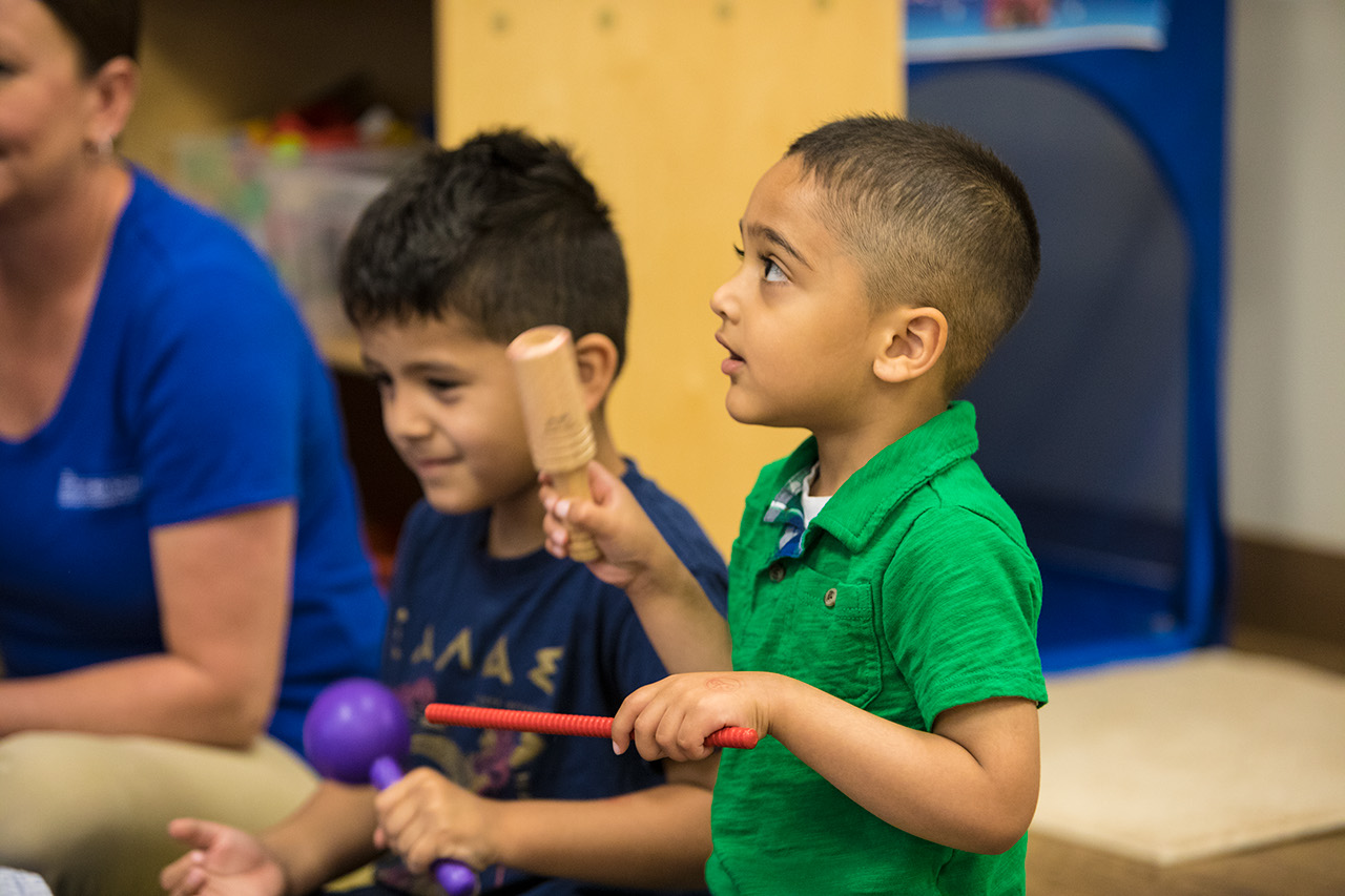 A boy plays with a percussive musical instrument within a larger group of children.