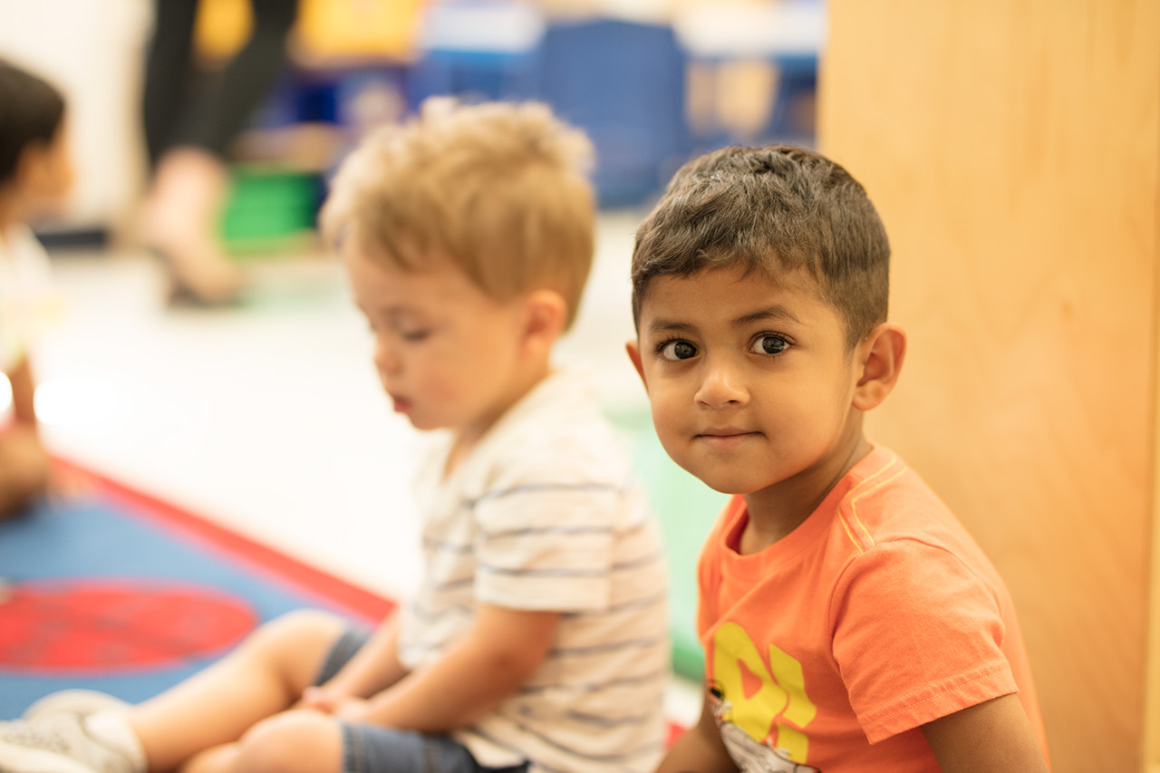 Two young children sitting on the floor. One looks at the camera with a little smirk.