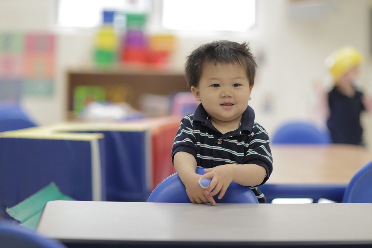 A toddler standing next to a table with chairs