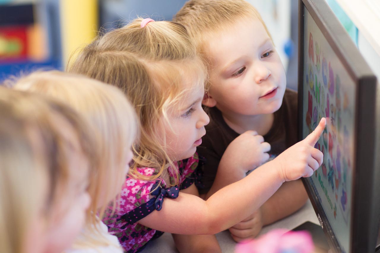 A group of young girls interact with a computer monitor in a Computer Lab.